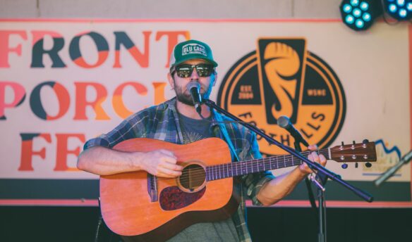 Man on stage with guitar, with Front Porch Fest sign in background